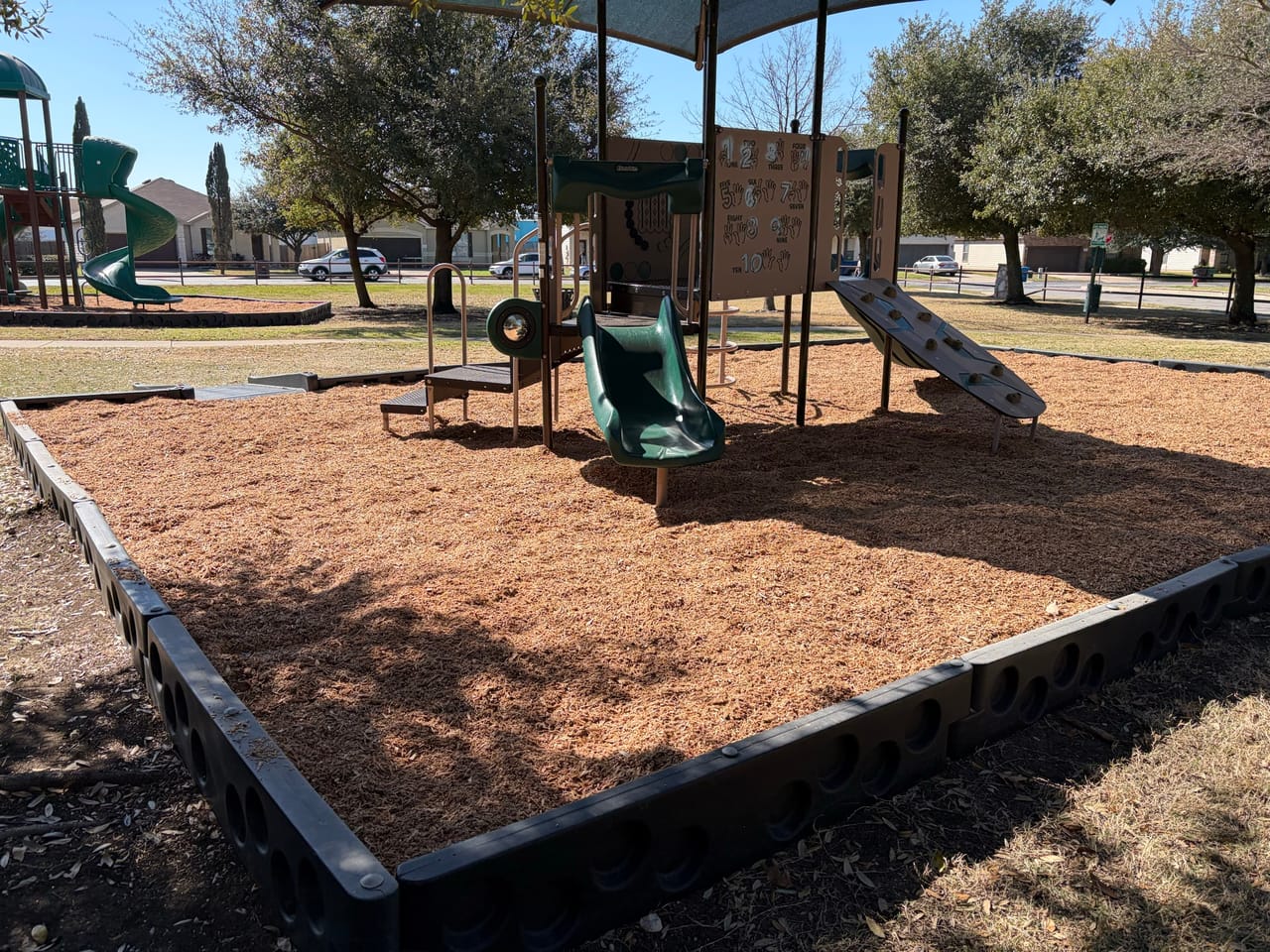 Freshly mulched playground bed with slide and swings in sun in Bastrop, TX