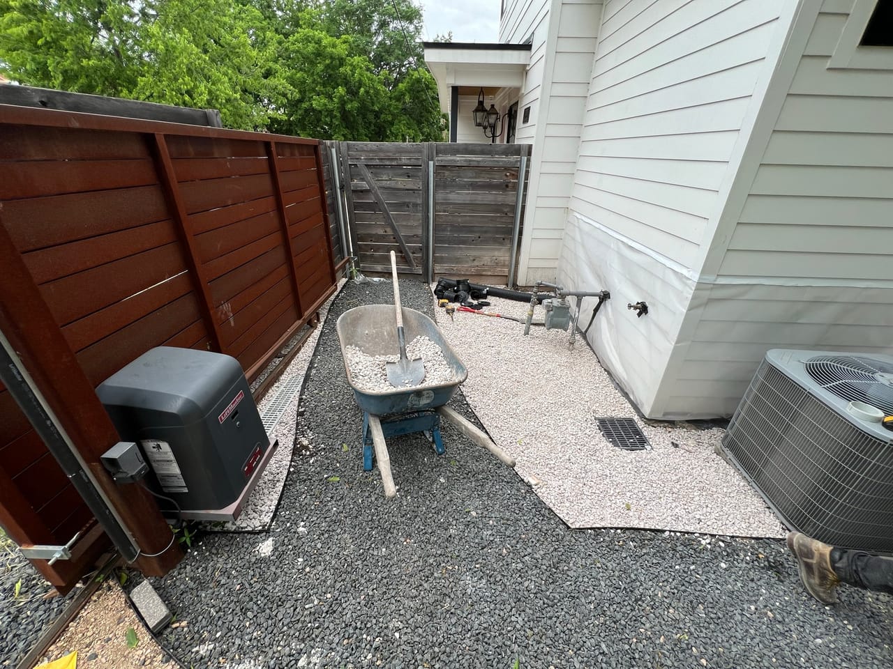 Side yard gravel spread with a wheelbarrow and AC unit nearby by Corral Bros in Central Texas