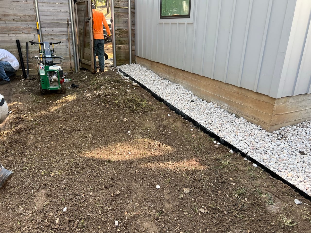 White gravel border along a house wall with worker and equipment in Buda, TX