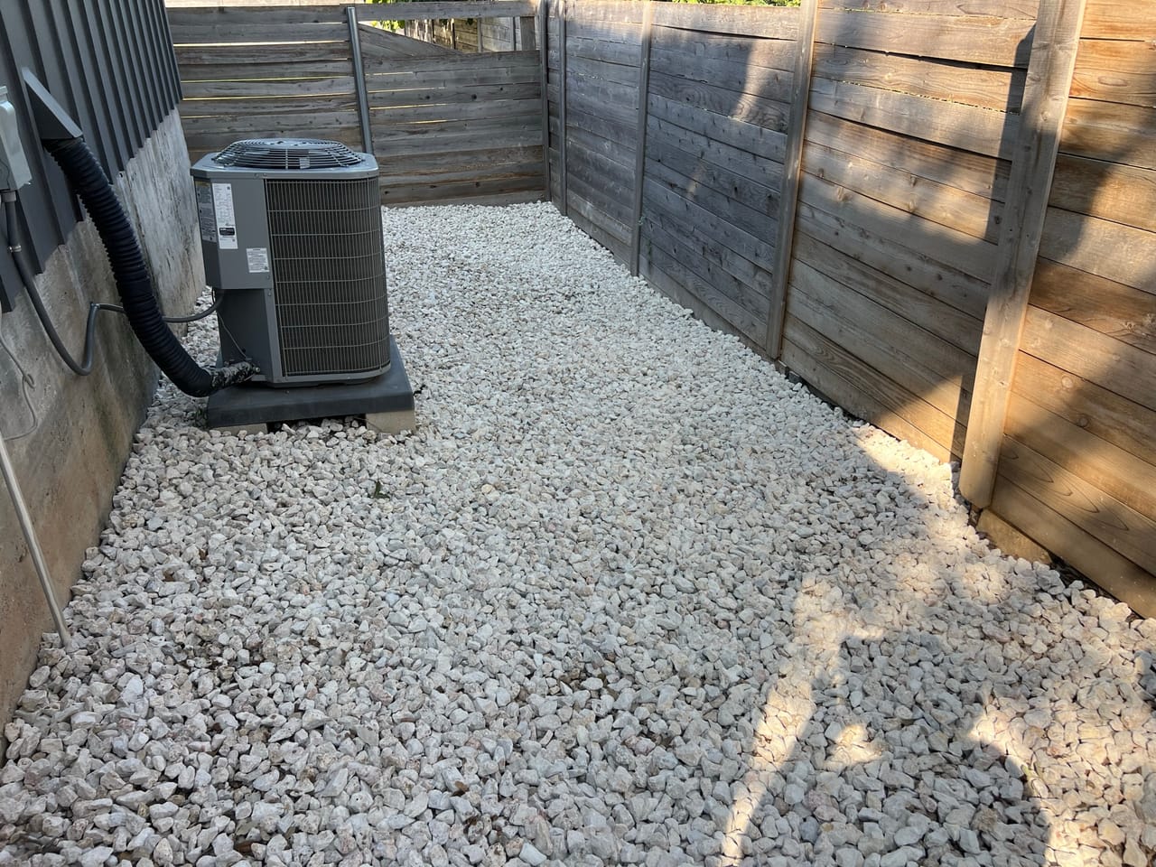 White river rock bed surrounding an AC unit in fenced corner in Cibolo, TX