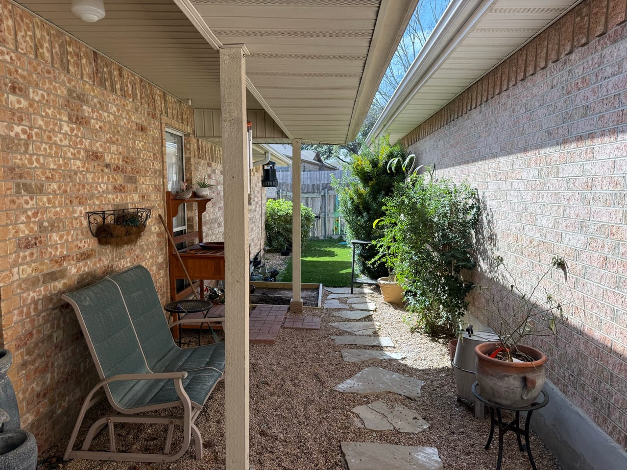 Covered brick porch with gravel side yard, potted plants and chairs in Leander, TX