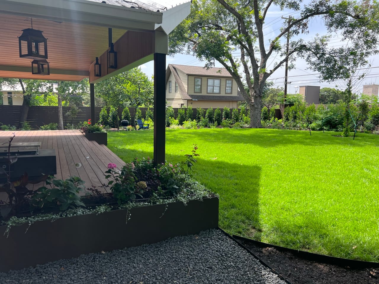 Covered patio with lanterns overlooking turf lawn and gravel border in Georgetown, TX