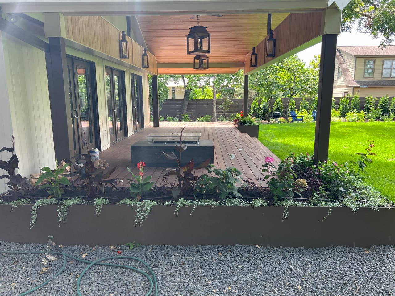 Covered porch with hanging lanterns, planter bed and green lawn in Buda, TX