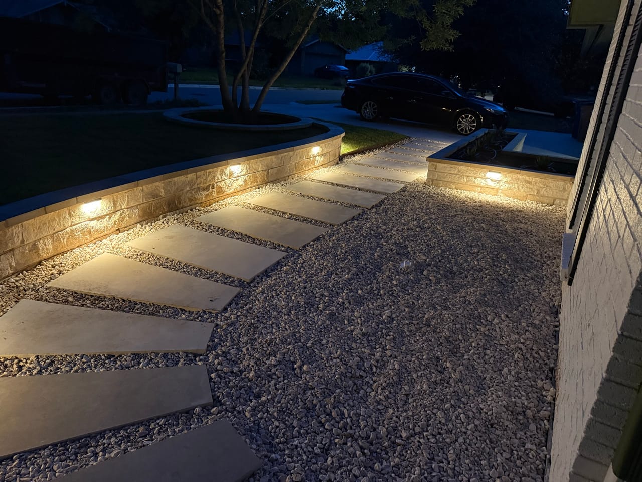 Dark night photo of a lit walkway and gravel bed in Round Rock, TX