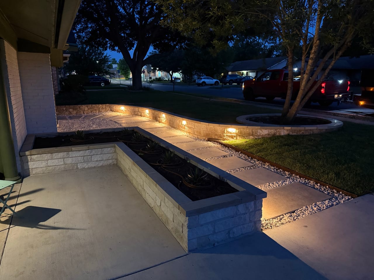 Evening shot of lit stone planter and walkway along the house in Buda, TX