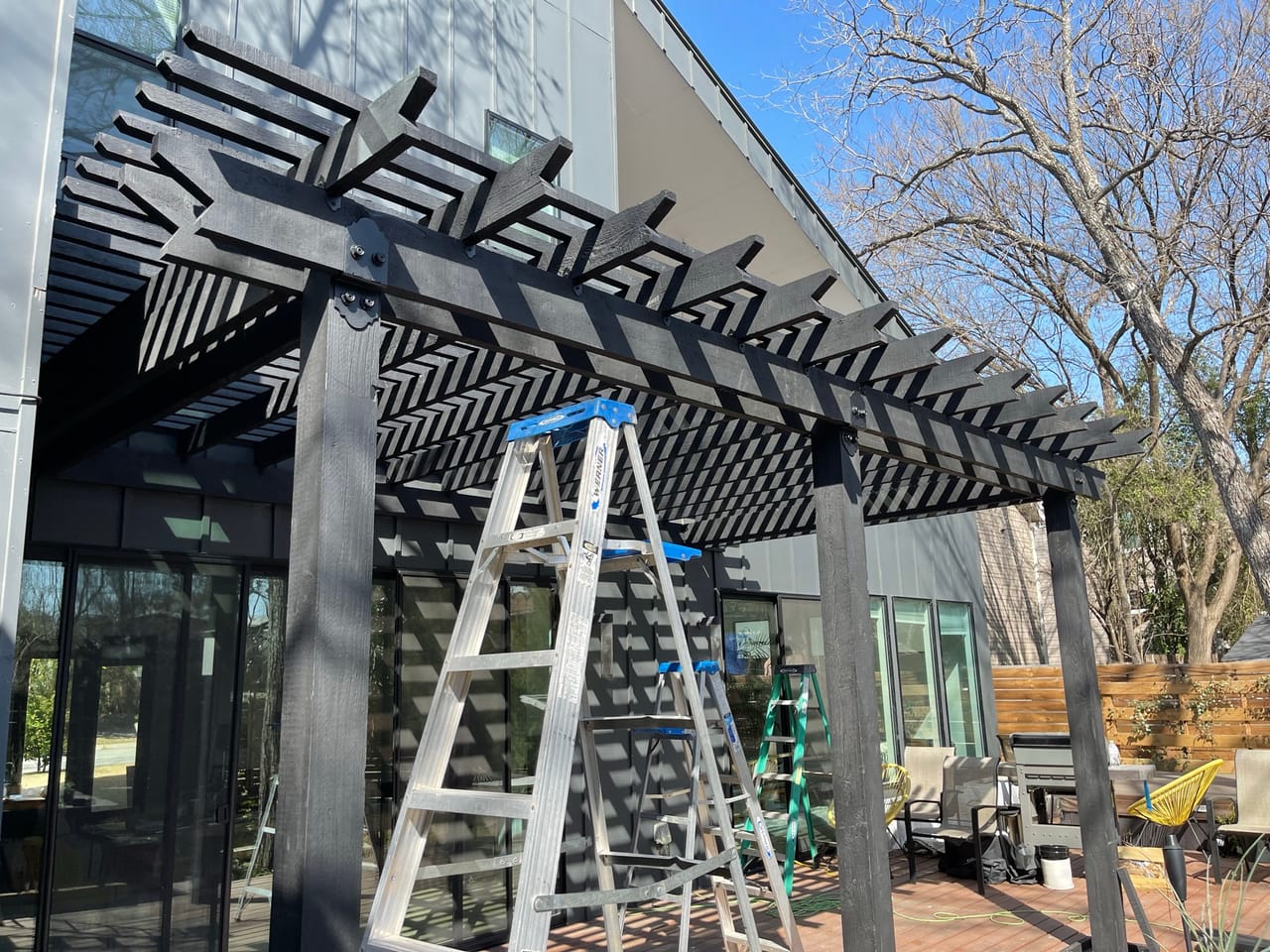 Ladder set under a black pergola being finished at modern house in Buda, TX