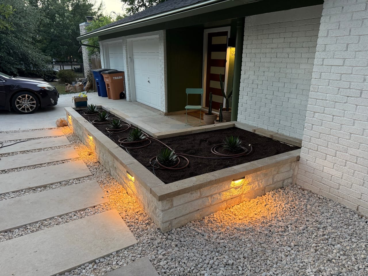 Lit raised planter beds and wide concrete walkway at dusk in Leander, TX