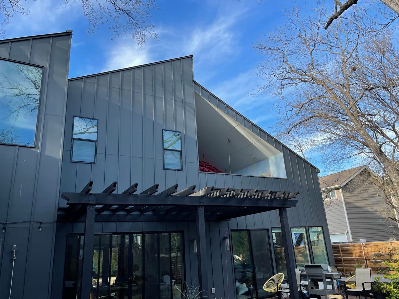 Modern dark metal home with black pergola under clear blue sky in Kyle, TX