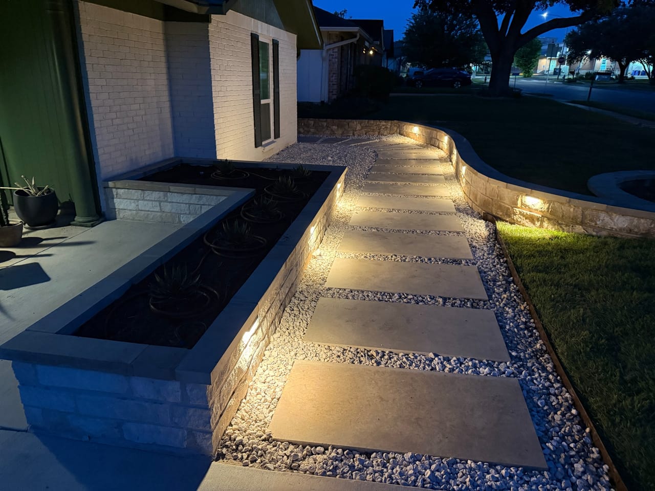 Night view of a lit walkway with planter wall and gravel bed in Round Rock, TX