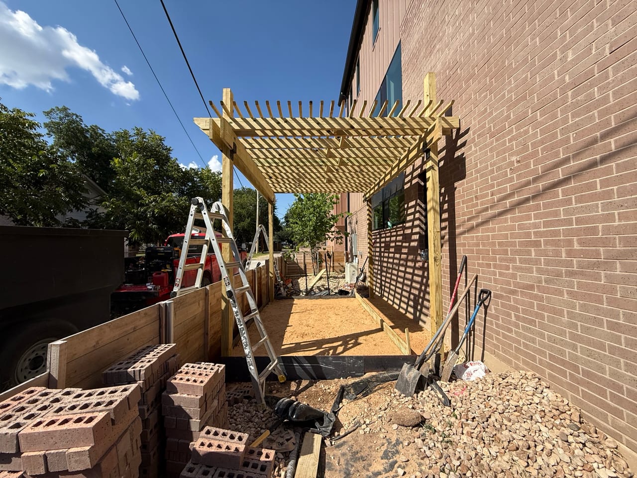 Pergola with lattice roof and stacked brick pallets in side yard in Buda, TX