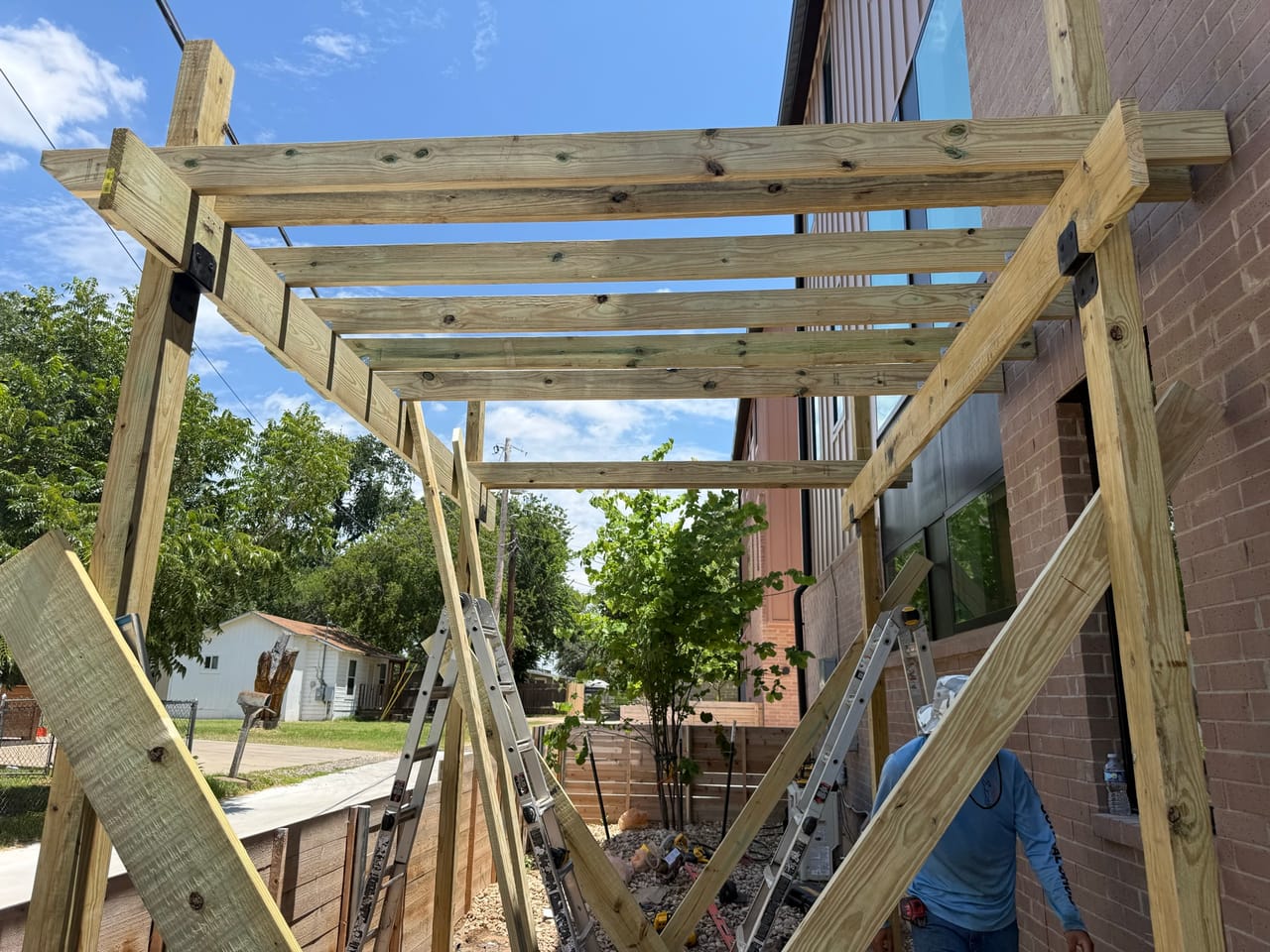 Pergola post and beam framing braced beside the brick house in Maxwell, TX