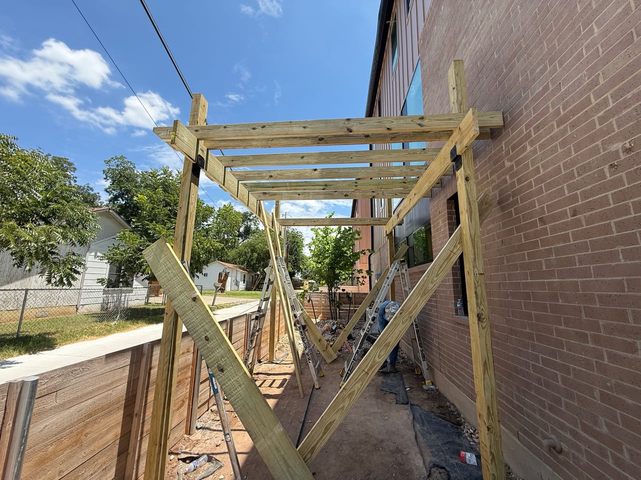 Wood pergola frame going up against a brick house wall in Georgetown, TX