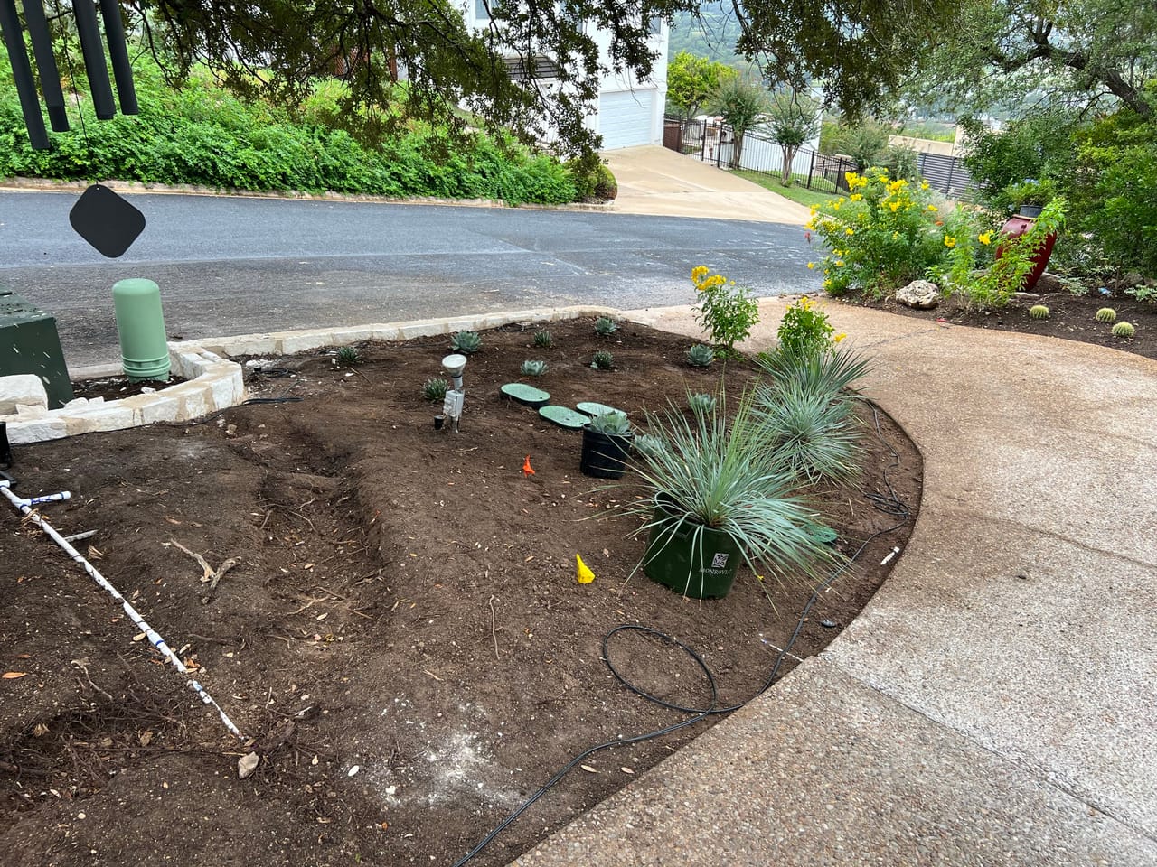 Fresh planting bed with new shrubs curving along a paved driveway by Corral Bros in Central Texas