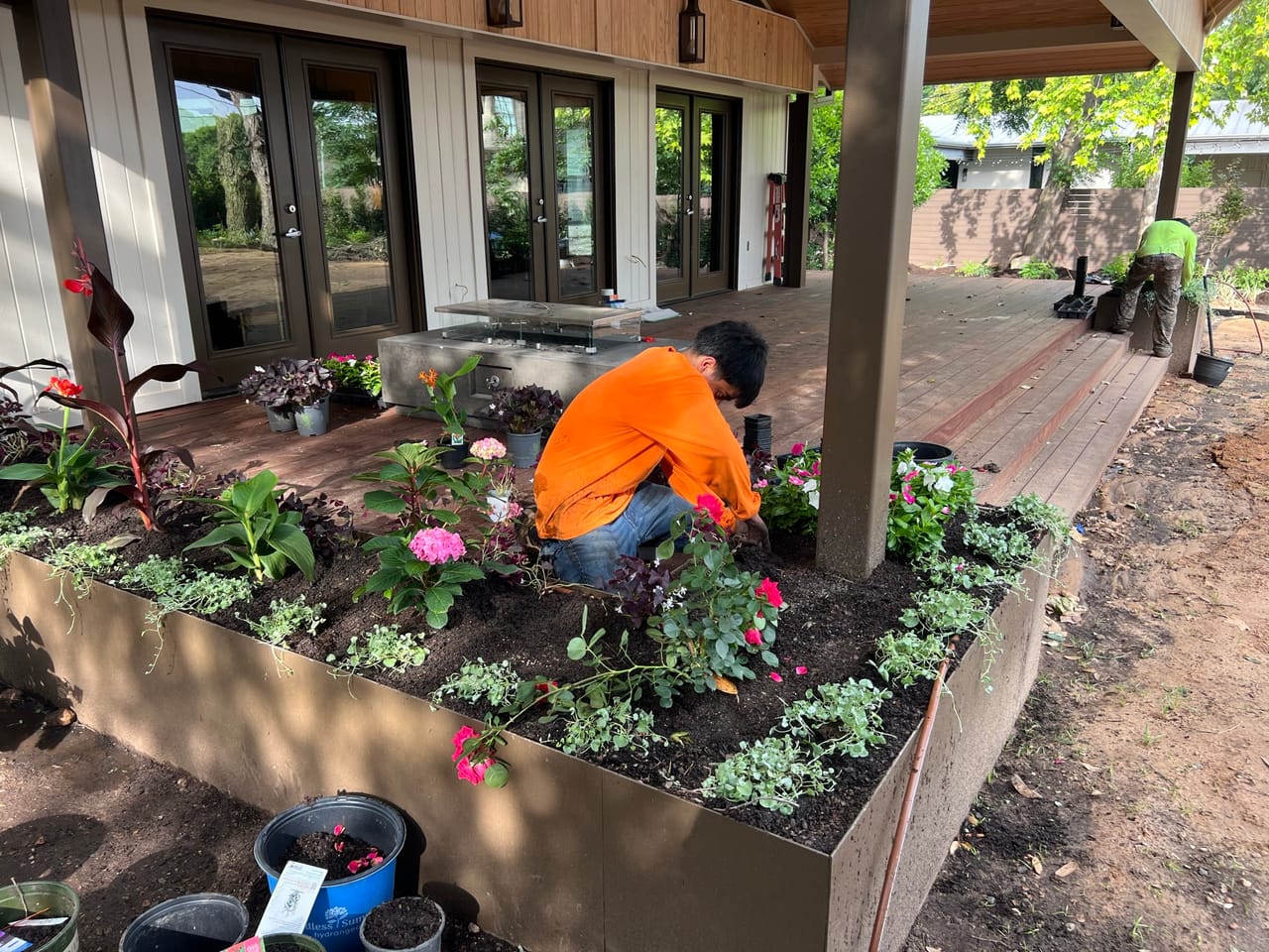 Wider shot of a worker planting a raised bed by patio doors by Corral Bros in Central Texas