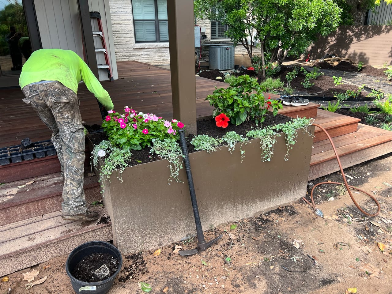 Worker in green shirt planting flowers in a metal planter box by Corral Bros in Central Texas