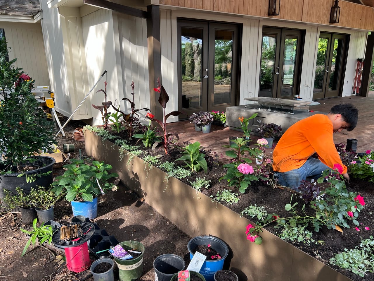 Worker planting colorful flowers in a long steel raised planter bed in Leander, TX