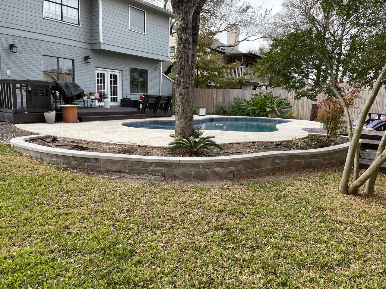Backyard pool ringed by a new curved stone edging and lawn in Leander, TX