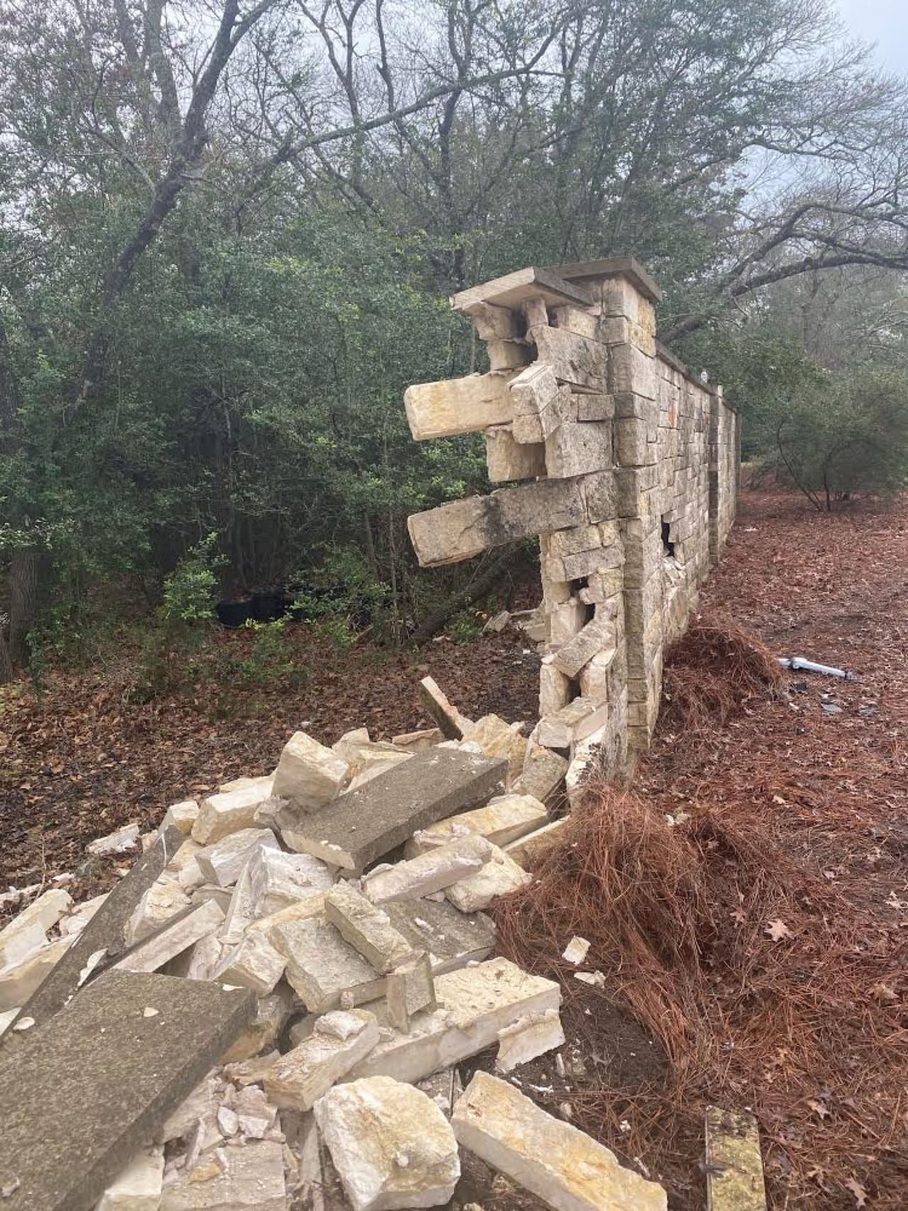 Collapsed stone pillar and rubble pile at a wooded property edge by Corral Bros in Central Texas