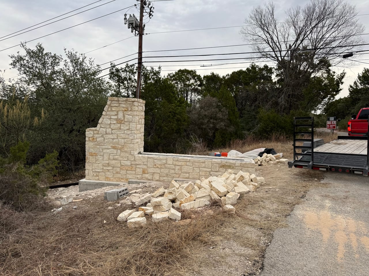 Completed limestone wall section with cut stone piled in front by Corral Bros in Central Texas