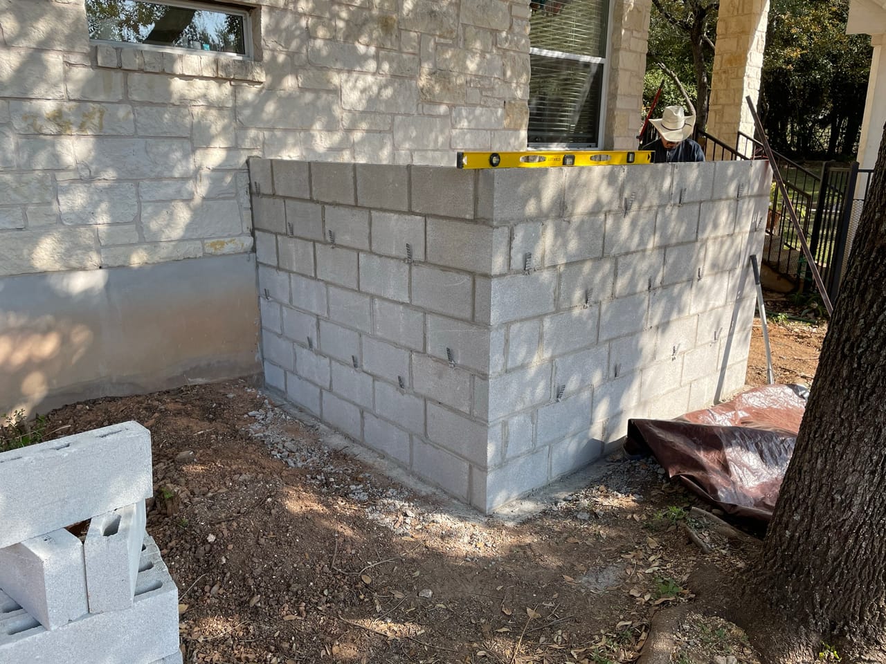 Corner of a new stone block wall with blocks and tarp staged in Bastrop, TX