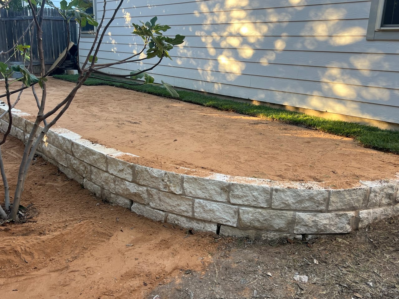 Curved limestone block retaining wall finished around a fresh planting bed in Georgetown, TX