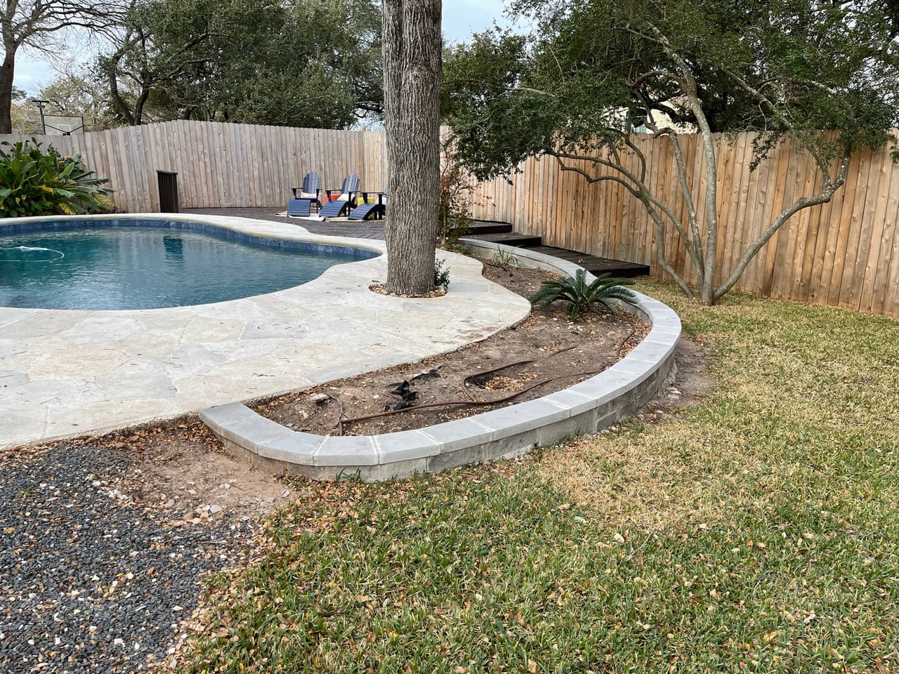 Curved stone border wall edging a pool deck and mulch bed in Buda, TX