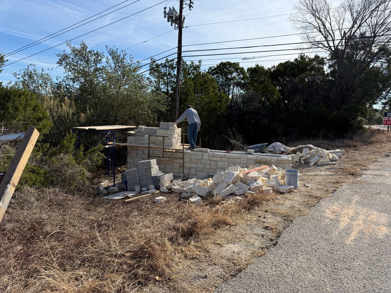 Limestone entry wall under construction beside a gravel drive by Corral Bros in Central Texas