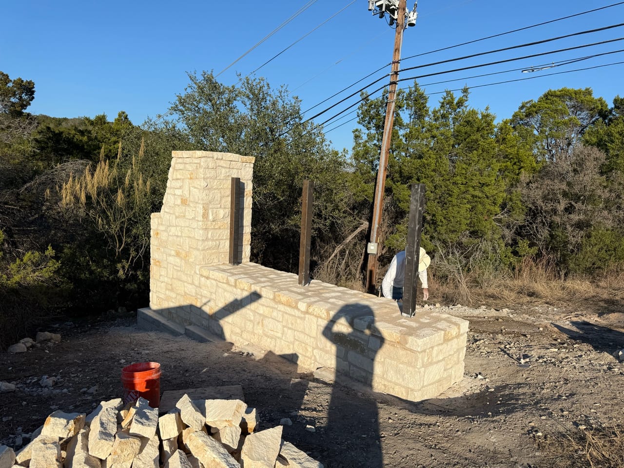 Limestone monument wall in progress with cut stone stacked nearby by Corral Bros in Central Texas