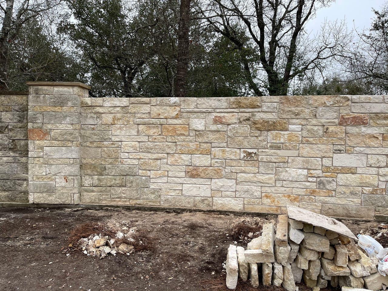 Long new stone veneer wall with leftover block stacked at the base by Corral Bros in Central Texas