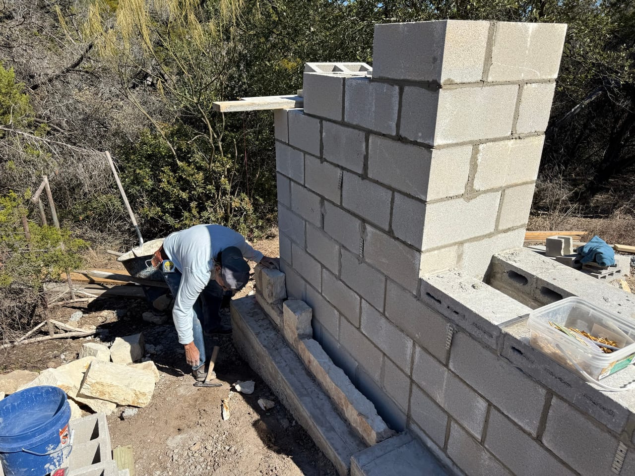 Mason bending to set block on a tall cinder block wall by Corral Bros in Central Texas