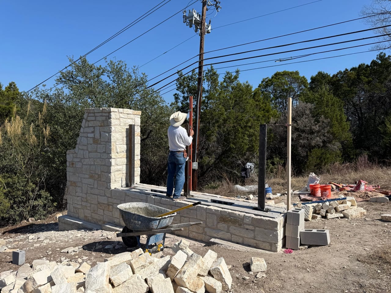 Mason at limestone entry wall with wheelbarrow and mortar tubs by Corral Bros in Central Texas