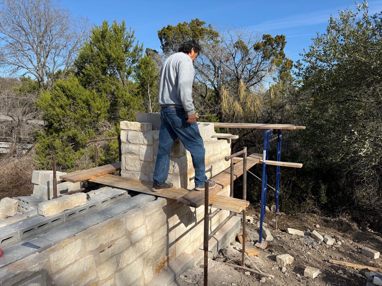 Mason on a plank scaffold laying limestone on a wall by Corral Bros in Central Texas