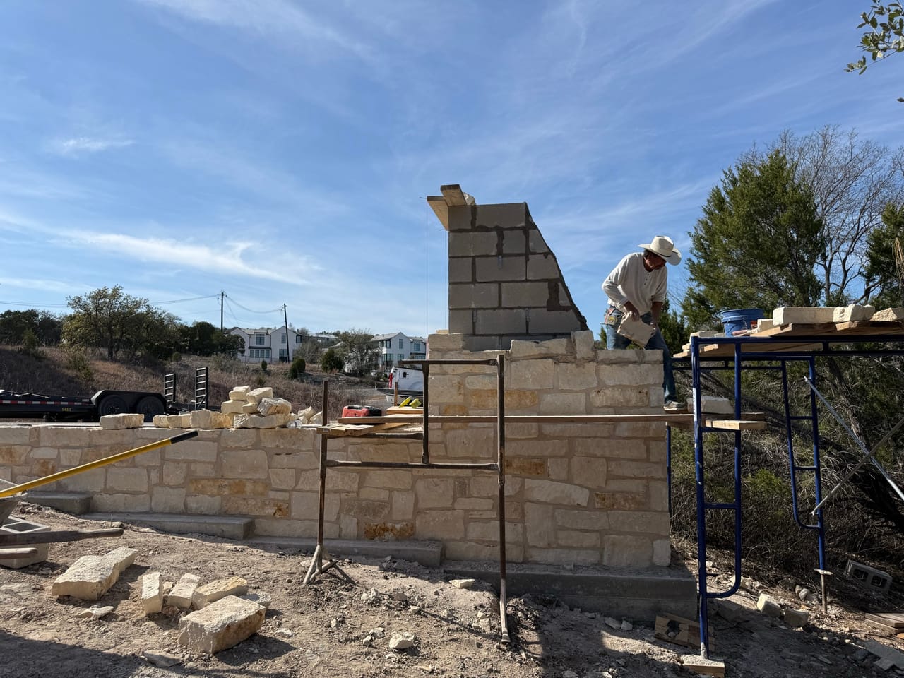 Mason setting block on a limestone entrance monument wall by Corral Bros in Central Texas