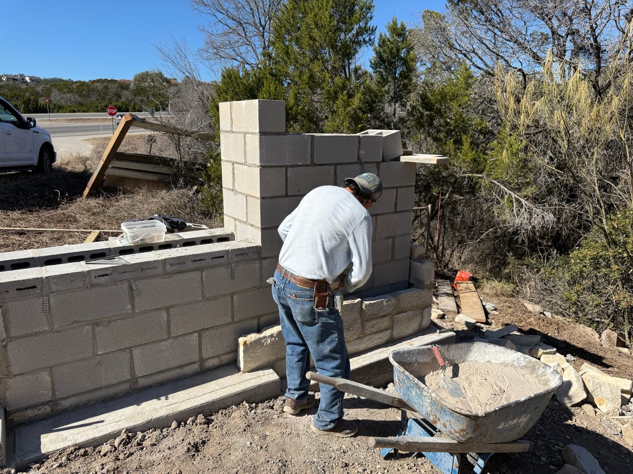 Mason working a block wall with wheelbarrow of mortar beside him by Corral Bros in Central Texas