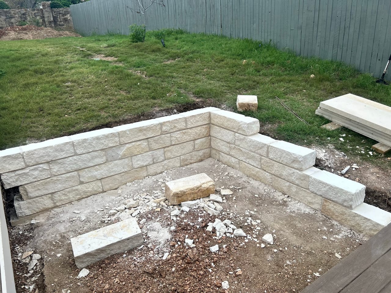 New limestone block retaining wall framing a sunken backyard patio area in New Braunfels, TX
