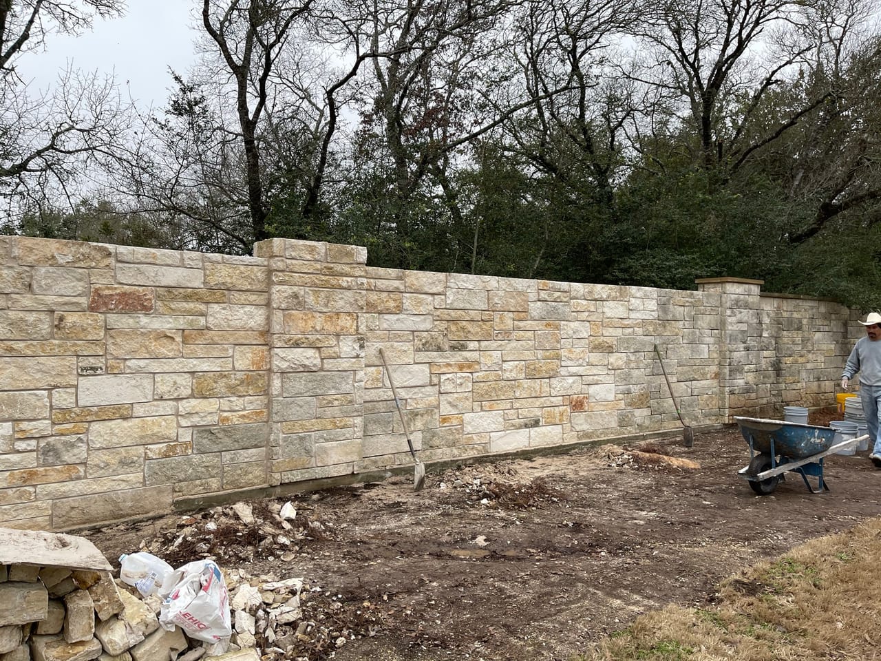 Same stone wall from the far end with a worker and wheelbarrow by Corral Bros in Central Texas