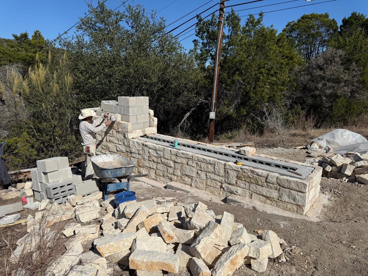 Stone wall build in progress with scattered limestone and mortar tubs by Corral Bros in Central Texas