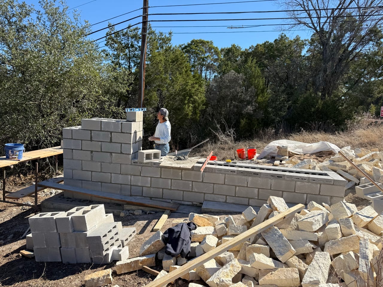 Worker laying concrete block wall with debris and lumber around by Corral Bros in Central Texas