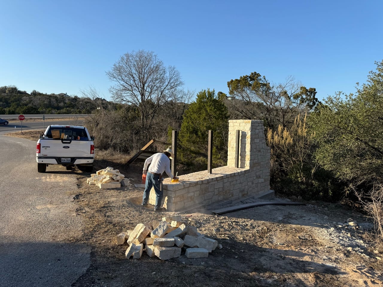 Worker at limestone wall with white pickup truck parked behind by Corral Bros in Central Texas