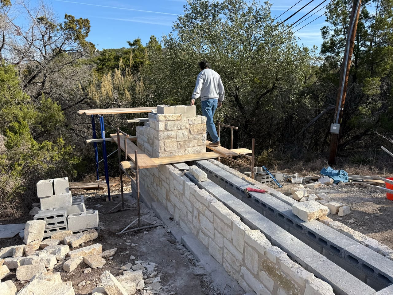 Worker on scaffold building a tall limestone entrance wall by Corral Bros in Central Texas