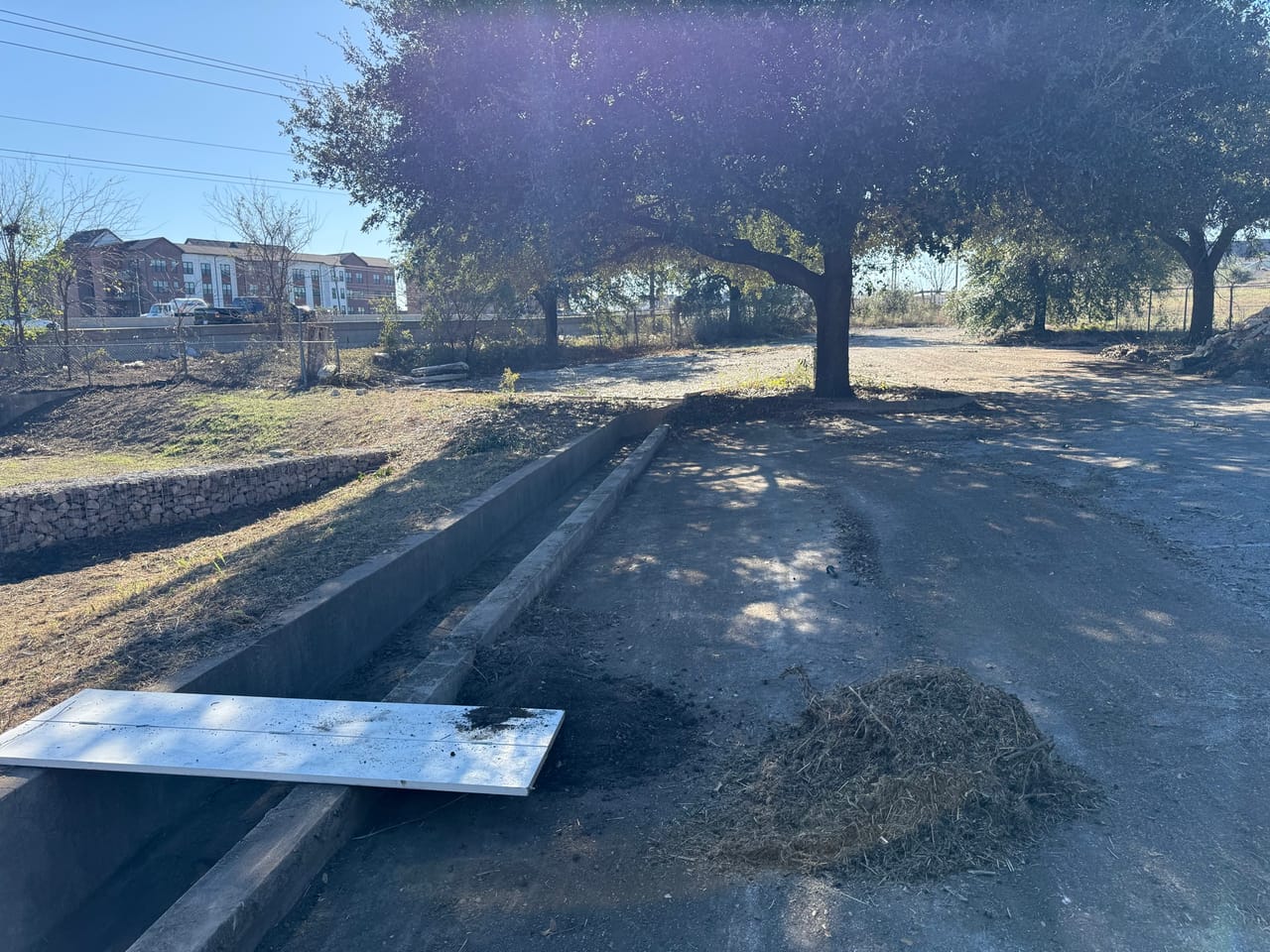 Long cleared strip with raked debris rows beside a paved lot in San Antonio, TX