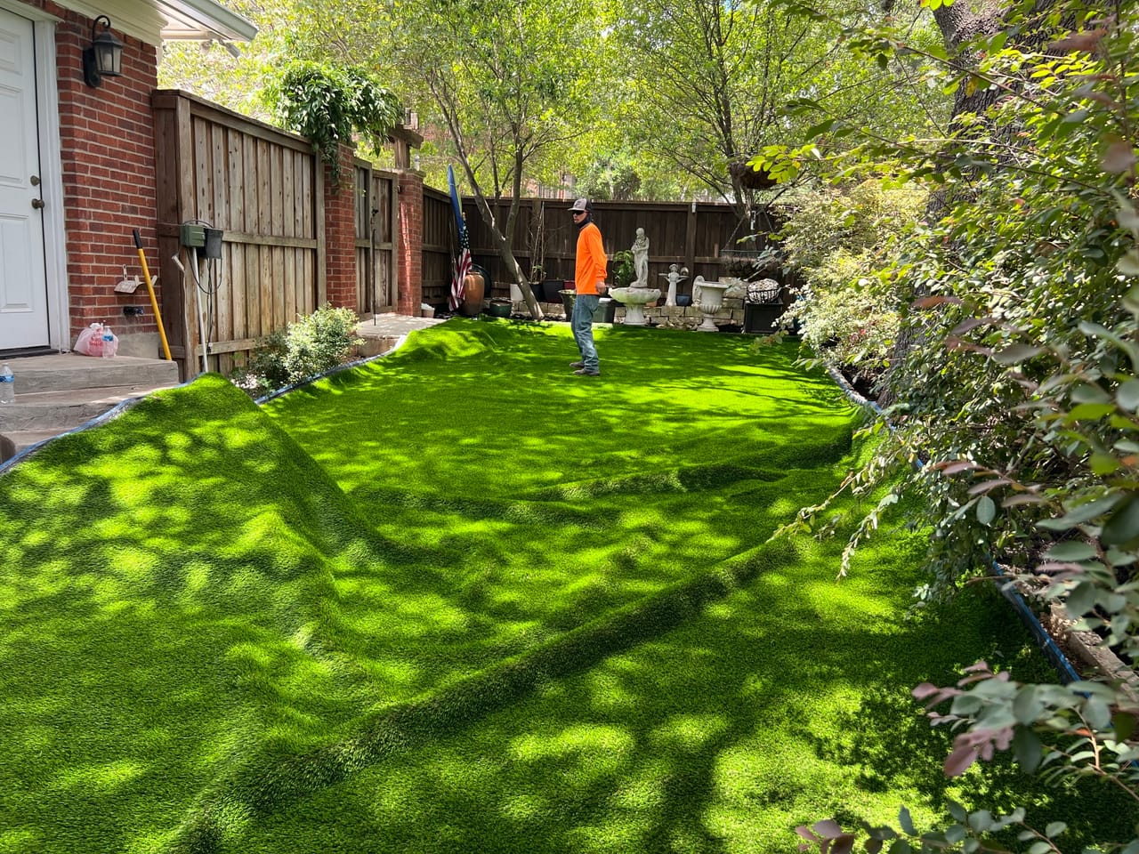 Bright green turf lawn finished in a fenced backyard with worker in Central Texas