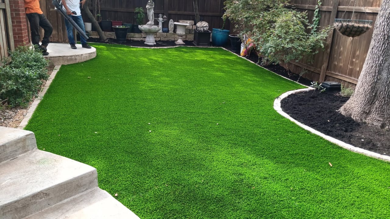Flawless turf lawn with curved mulch border and stone fountain by Corral Bros in Central Texas