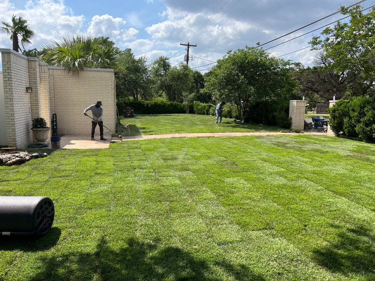 Green sod lawn with a lawn roller and crew by white walls by Corral Bros in Central Texas