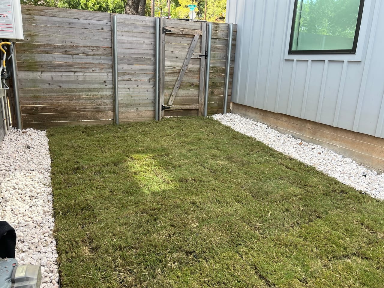 New sod backyard with wood fence and gate, white gravel strip in Lakeway, TX