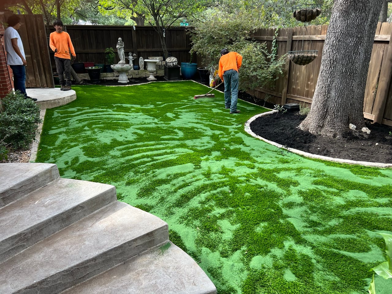 Two workers brushing in newly installed bright green artificial turf in Leander, TX
