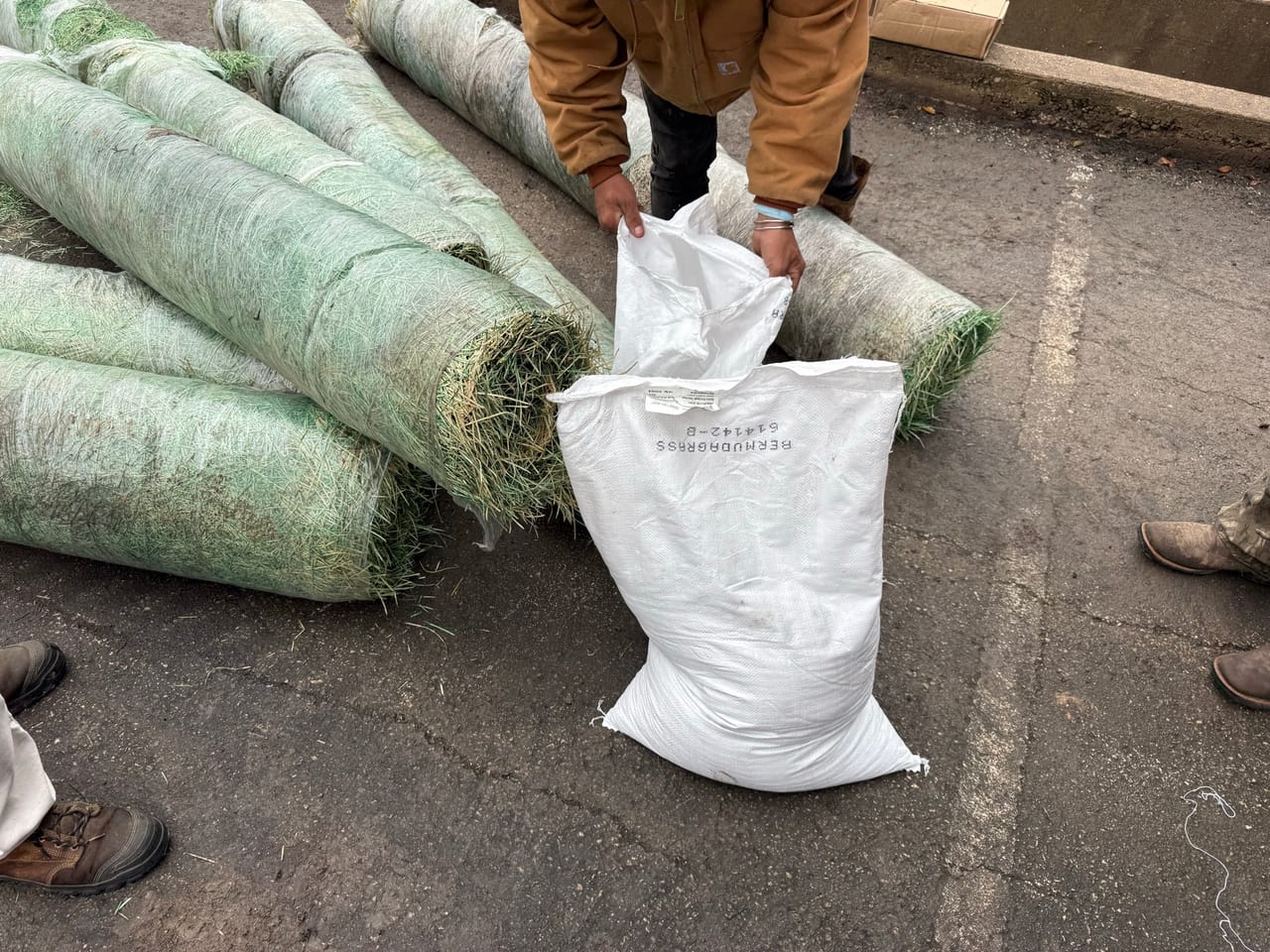 Worker setting down rolls of green erosion blanket beside a sandbag by Corral Bros in Central Texas