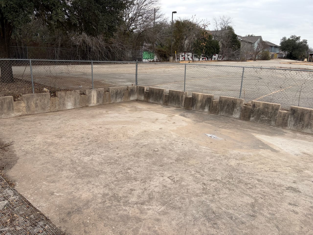Bare graded detention basin ringed by concrete walls and chain link by Corral Bros in Central Texas