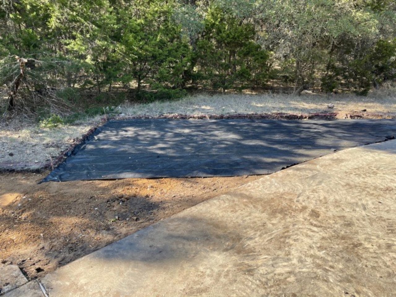 Black pond liner spread flat over a graded basin area in Leander, TX