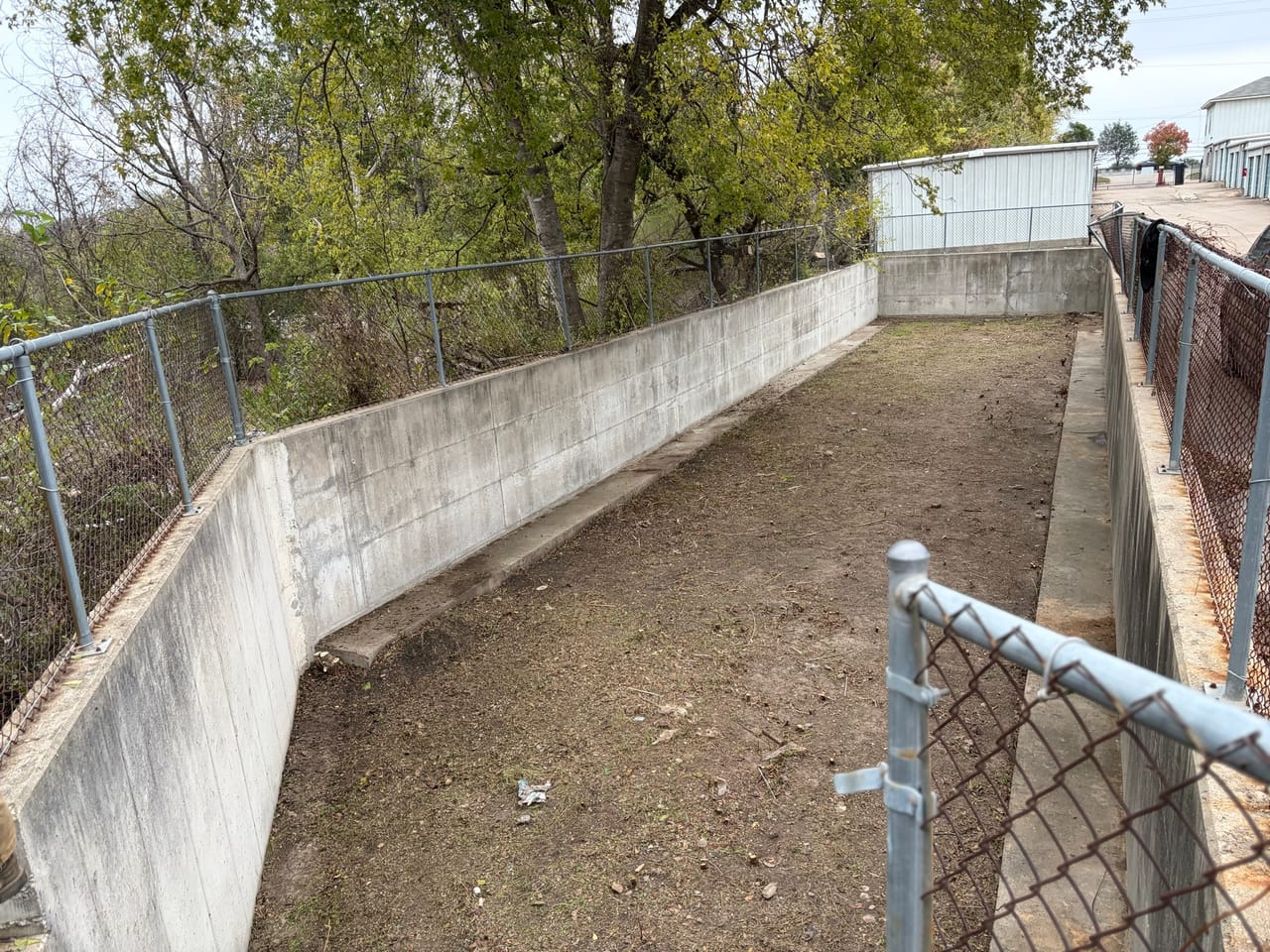 Cleaned rectangular concrete detention basin with graded dirt bottom and fence in Leander, TX